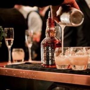 A bartender pouring a cocktail from a shaker into chilled cocktail glasses.